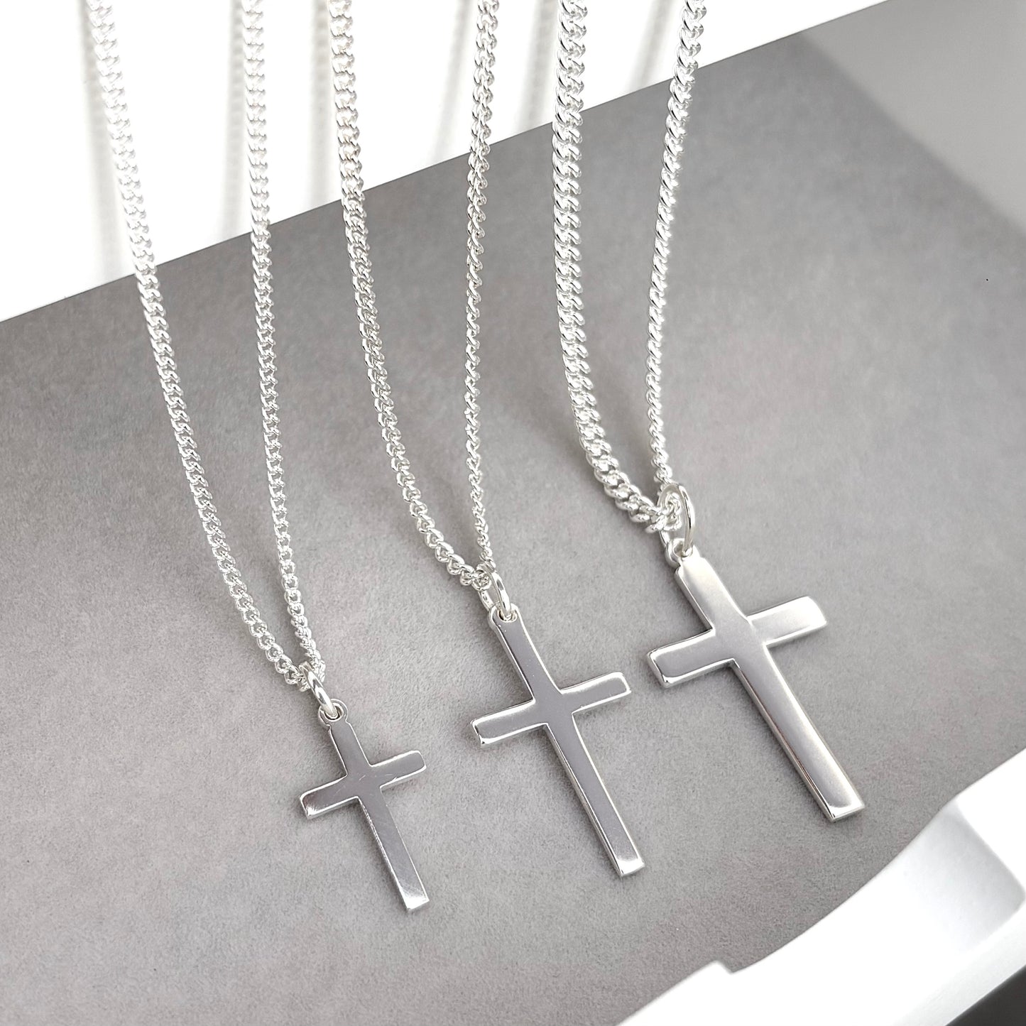 Polished sterling silver plain small, standard, and medium cross pendants on a curb chain