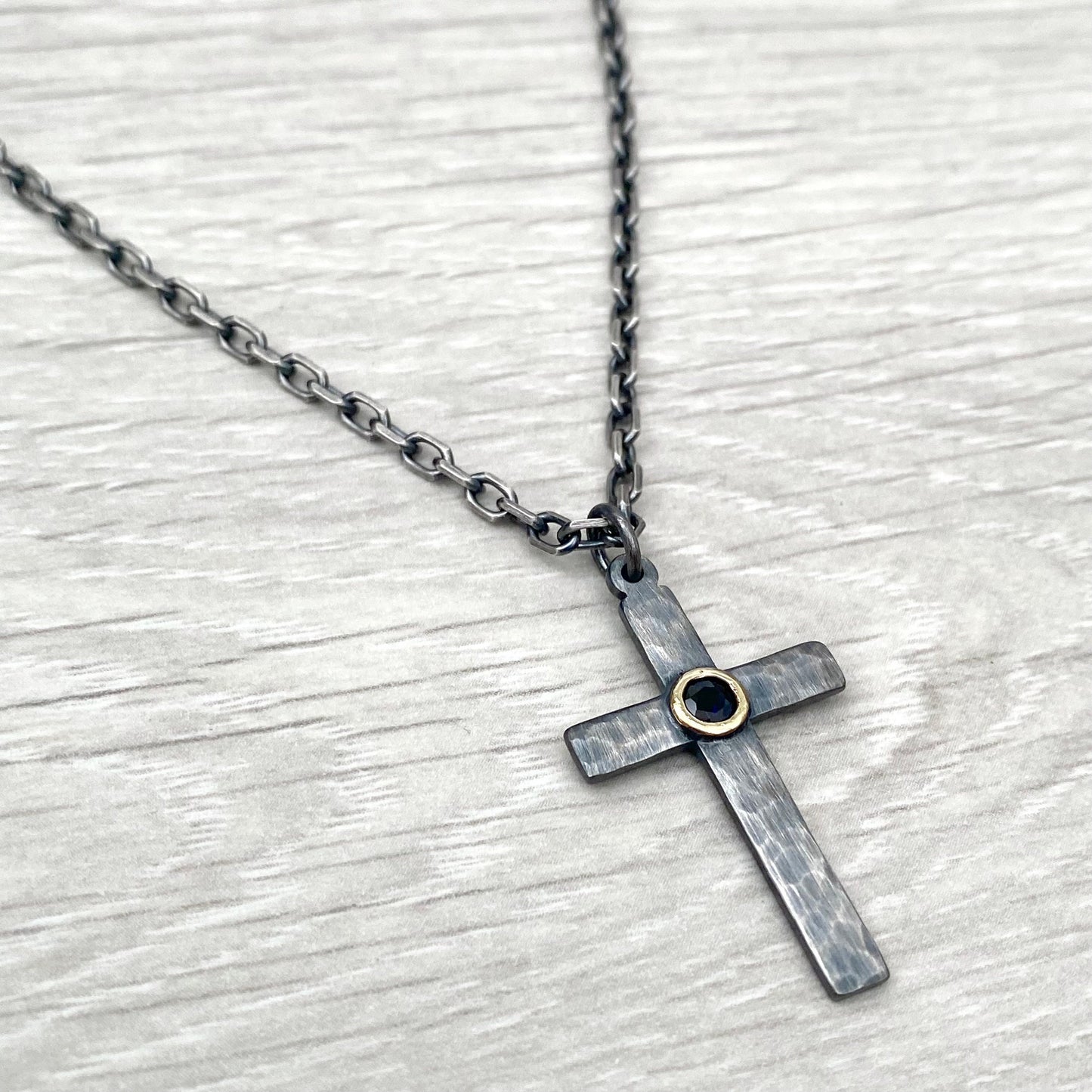 Oxidised solid sterling silver hammered medium size cross with a 9ct yellow gold set black sapphire on a diamond cut trace chain