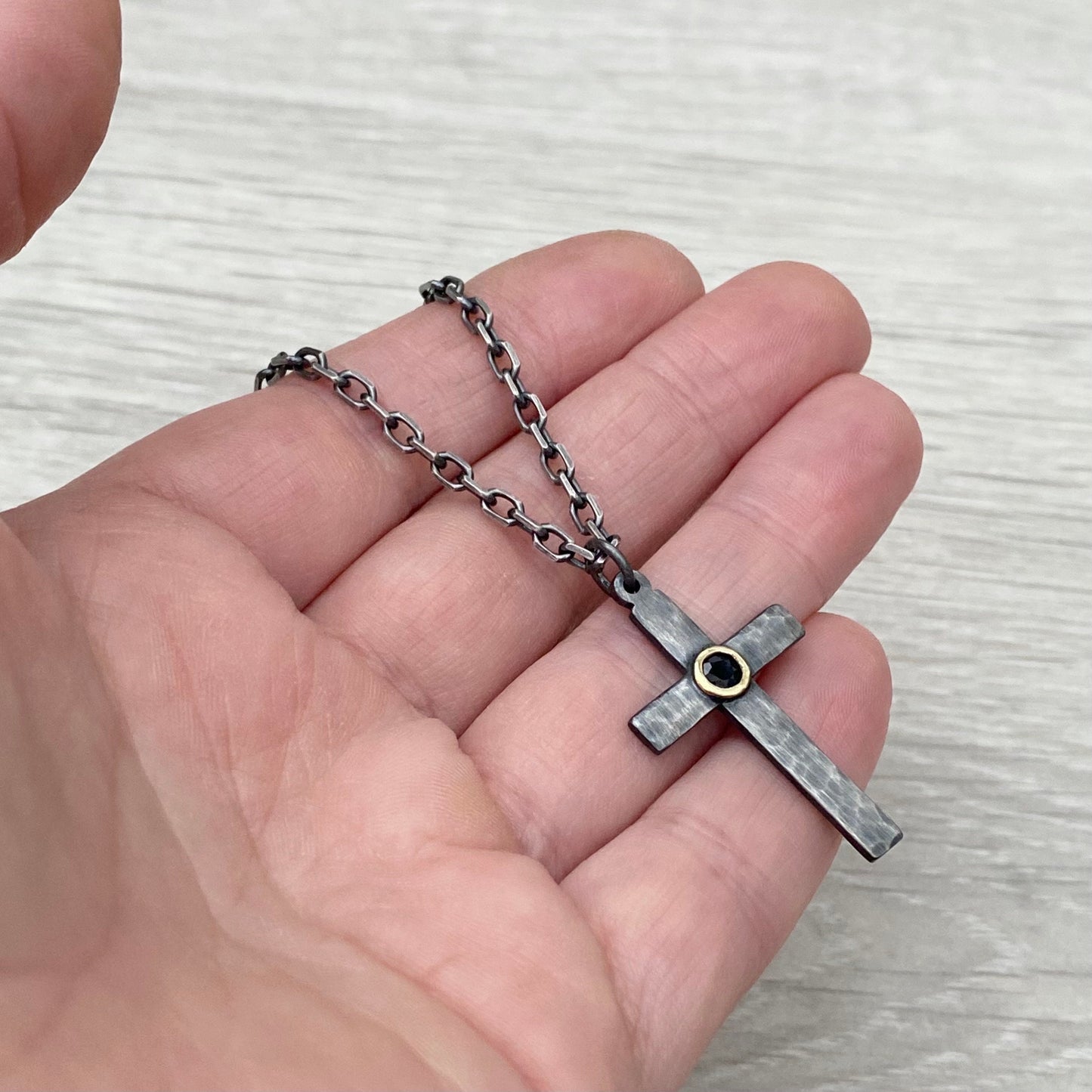 Oxidised solid sterling silver hammered medium size cross with a 9ct yellow gold set black sapphire on a diamond cut trace chain