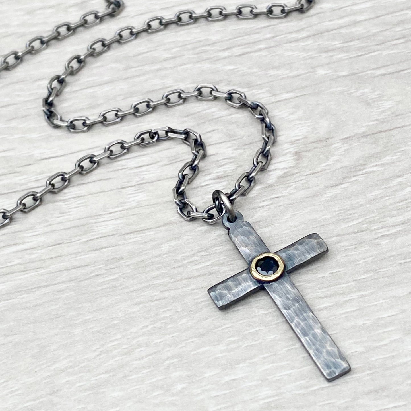 Oxidised solid sterling silver hammered medium size cross with a 9ct yellow gold set black sapphire on a diamond cut trace chain