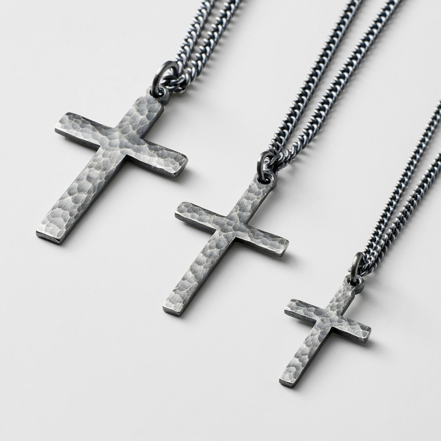 Oxidised or polished solid silver hammered finish small, standard, and medium cross pendants on a curb chain